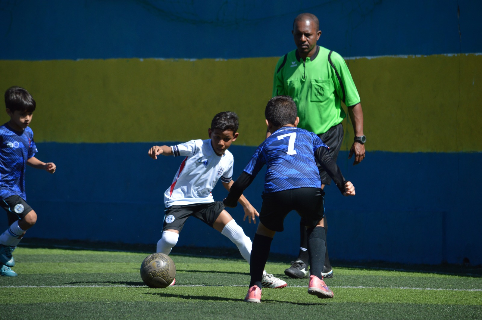 Alunos disputando a bola com acompanhamento do árbitro