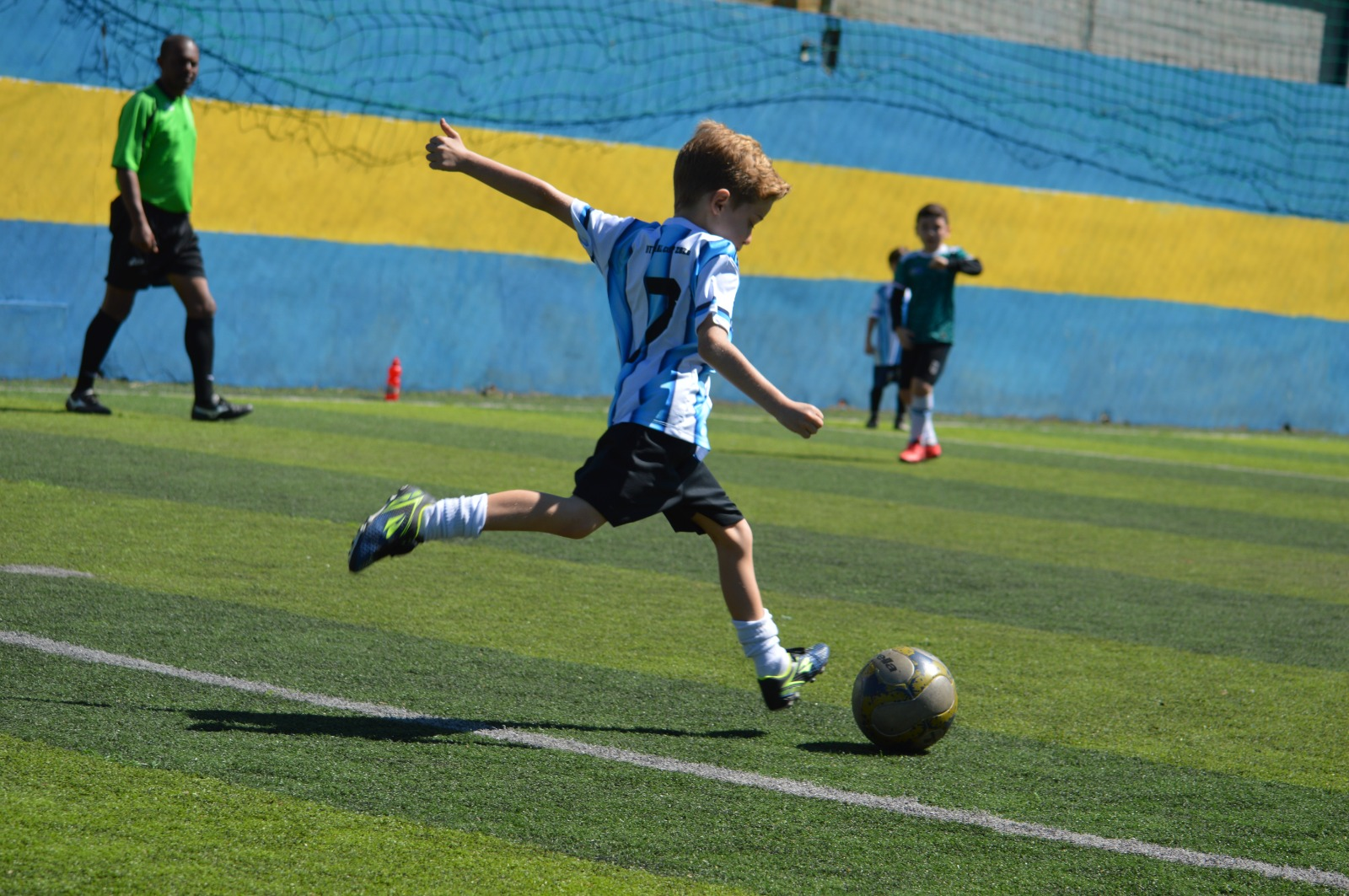 Criança chutando a bola durante treino da CJR Esportes